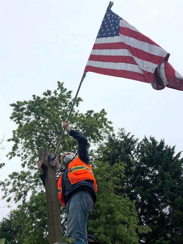 With Roy Baumgartner (not pictured) holding the ladder, Ken Gresset raises a flag on Vashon Highway on Monday morning (Tom Hughes Photo).