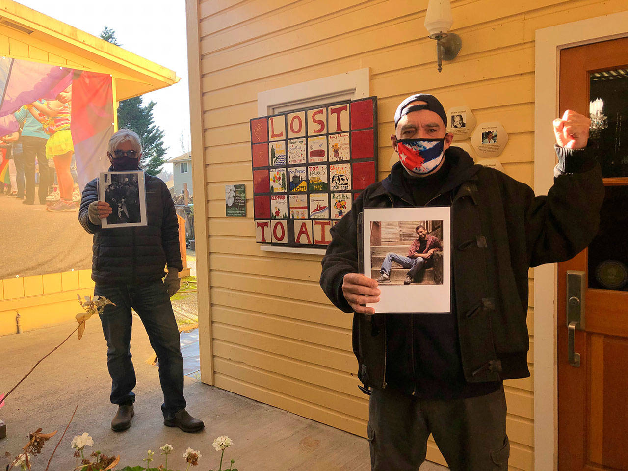 Tom Hughes Photo
Peter Serko and Chris Boscia (in foreground) hold photos of their heroes, David Serko and Spencer Cox, in the courtyard exhibit of Vashon Heritage Museum’s “In and Out: Being LGBTQ on Vashon.” Peter’s photo shows his brother David being arrested in New York in 1988, at a protest, one month after his diagnosis. The courtyard exhibit, still open to the public, features a tile “quilt,” created by Vashon High School students as part of Vashon World AIDS Day in 2018.