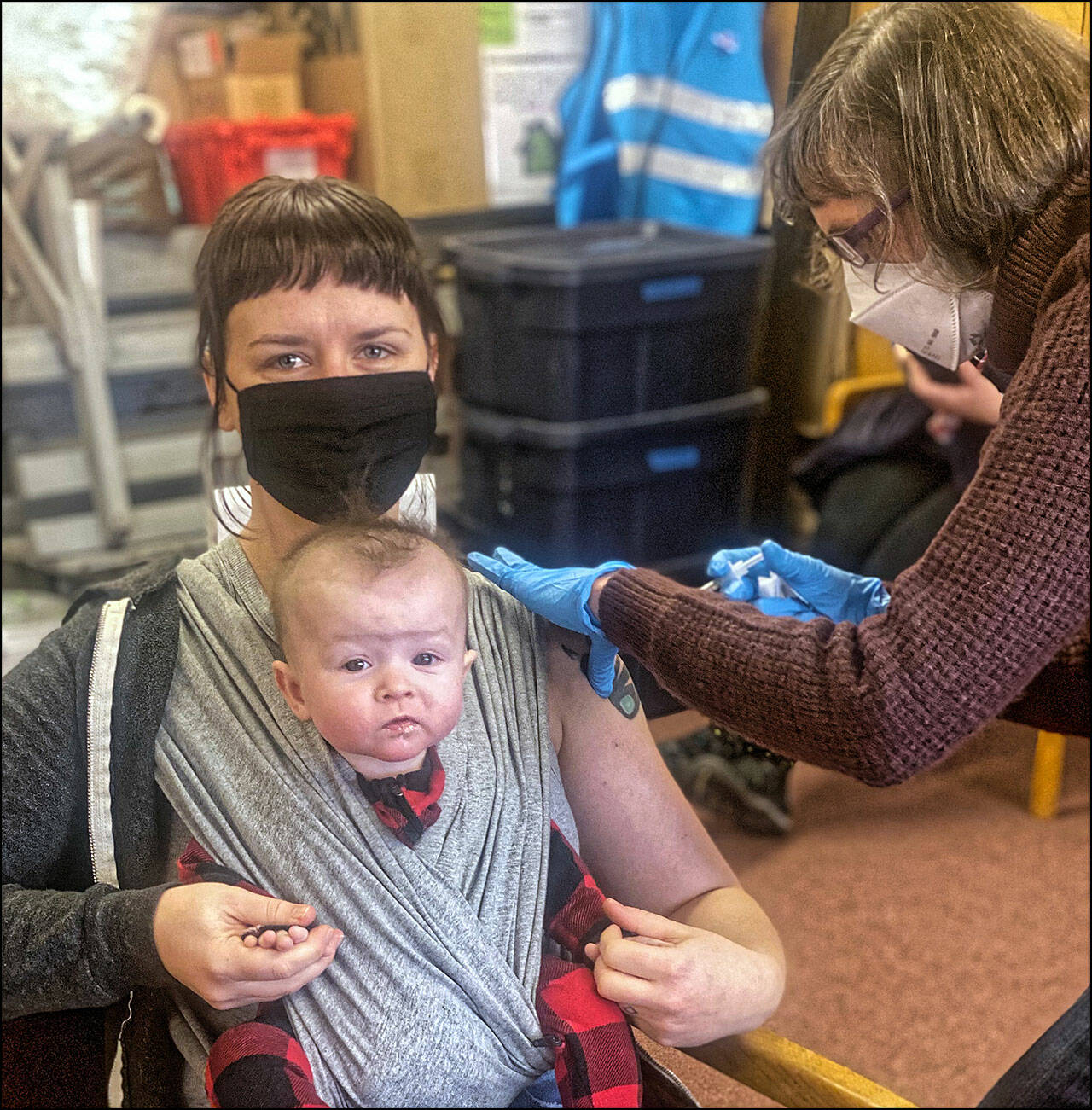 (Marijke van Heeswijk Photo) It Has Been a Long Pandemic: Zoe Burkland got her vaccination months ago when she was pregnant with Hazel. Now, here’s Zoe getting her booster shot and she brought 6-month-old Hazel along. “I encourage everyone to get vaccinated and get their booster shots. That’s especially true for pregnant people,” Zoe said. “Protecting our babies is so important, and getting a COVID vaccine during pregnancy is the best way to keep them safe, now and once they’re born.” Also the mother of a 3-year-old who cannot yet receive a shot, Zoe said, “Please vaccinate your big kids, too! After all, vaccinating kids is the missing piece to substantially lower transmission and getting closer to normal for everyone.” Nurse Cece Reoux does the vaccination honors.