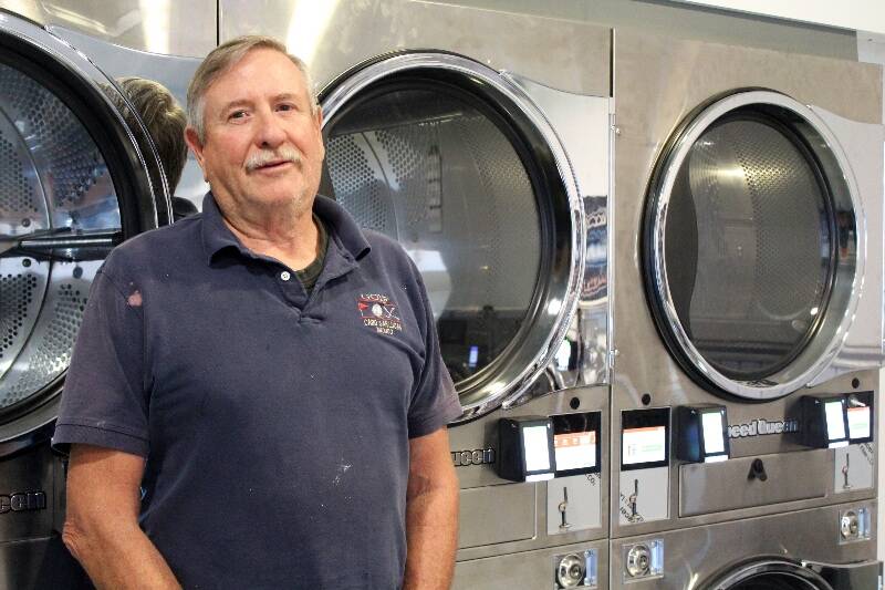 Dennis Morrow, a Port Orchard resident, is one of the co-owners of Vashon Laundry - pictured here next to some of the new washers at the business (Alex Bruell / The Beachcomber Photo).