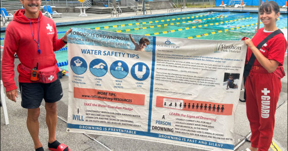 Megan Yeager (right), Vashon Park District lifeguard, swim instructor, and Vashon Seals Swim Team assistant coach, holds a banner of water safety tips with lifeguard colleague Michael “Wish” Wishkoski. “At a bare minimum, every child should learn how to float,” Yeager said. (Courtesy photo.)