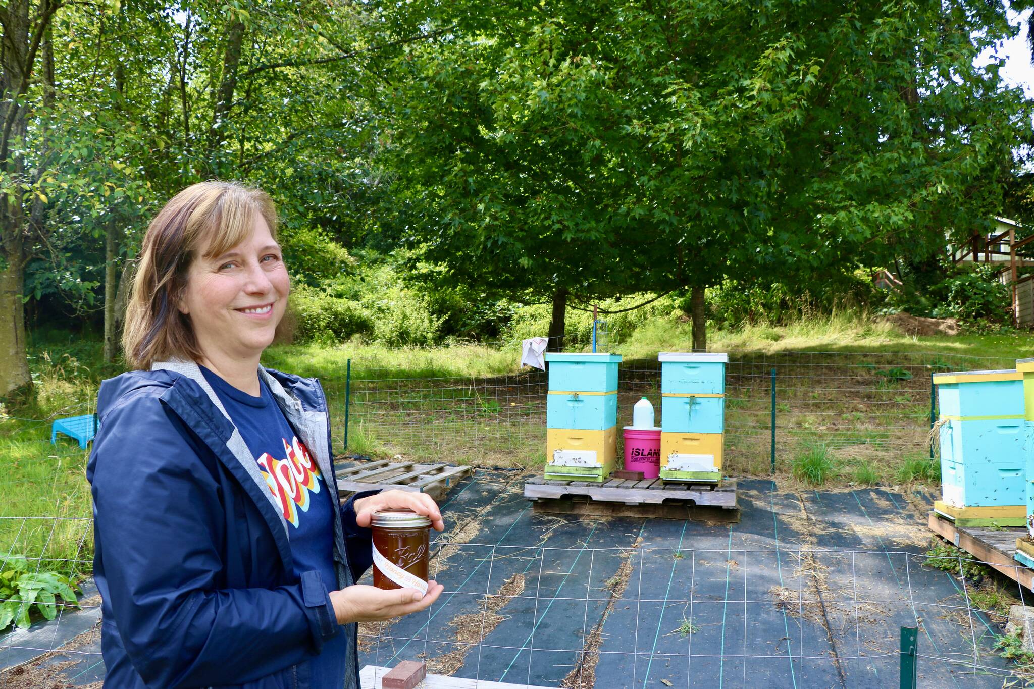 Islander Jenna Riggs holds a jar of honey next to her hives on Vashon Island. (Aspen Anderson photo.)