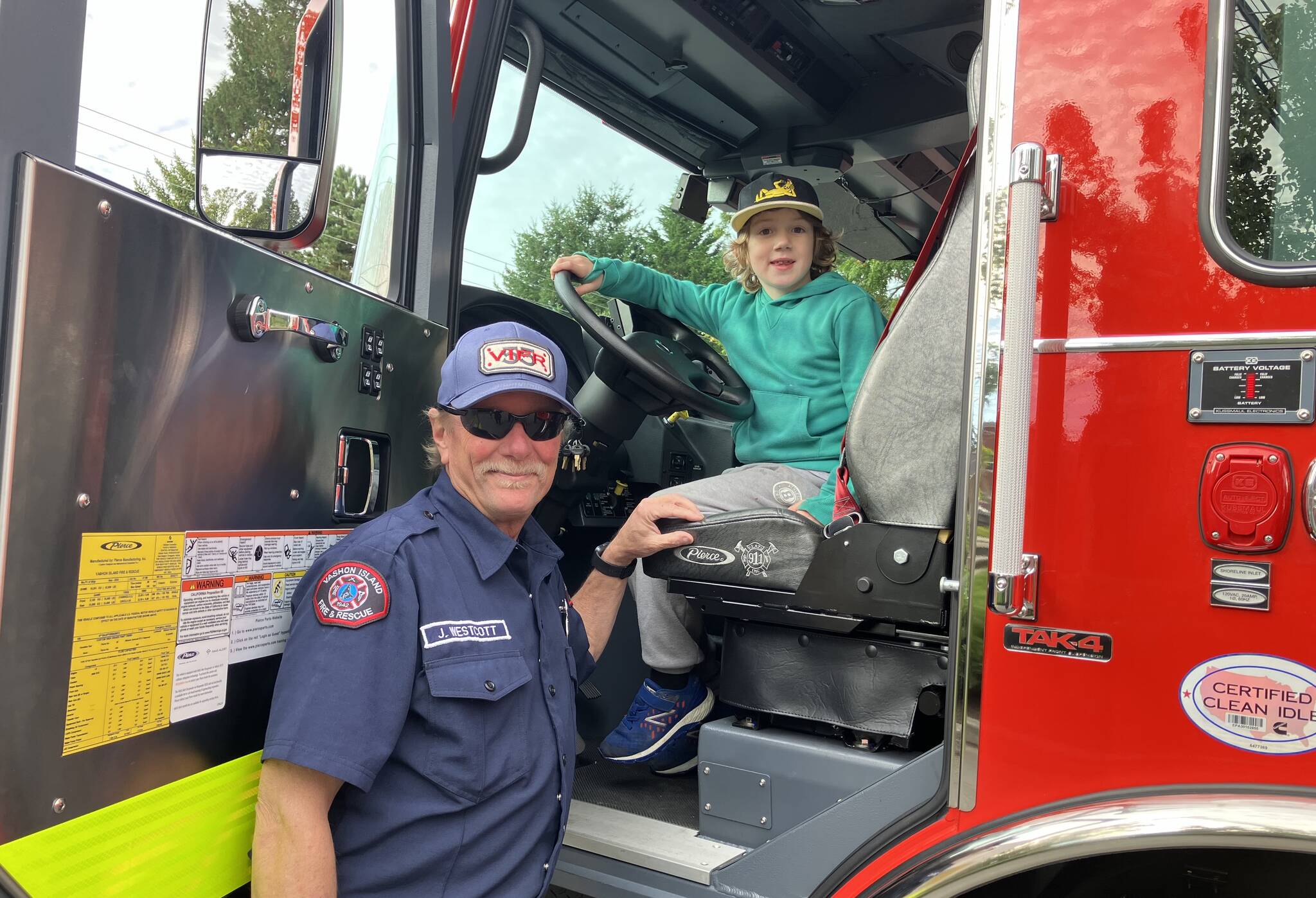 Oly Anderson perched behind the wheel of Vashon Island Fire District’s new fire engine at the district’s open house on Saturday, with volunteer firefighter/EMT Jim Westcott standing by to tell him all about it. (Elizabeth Shepherd photo)