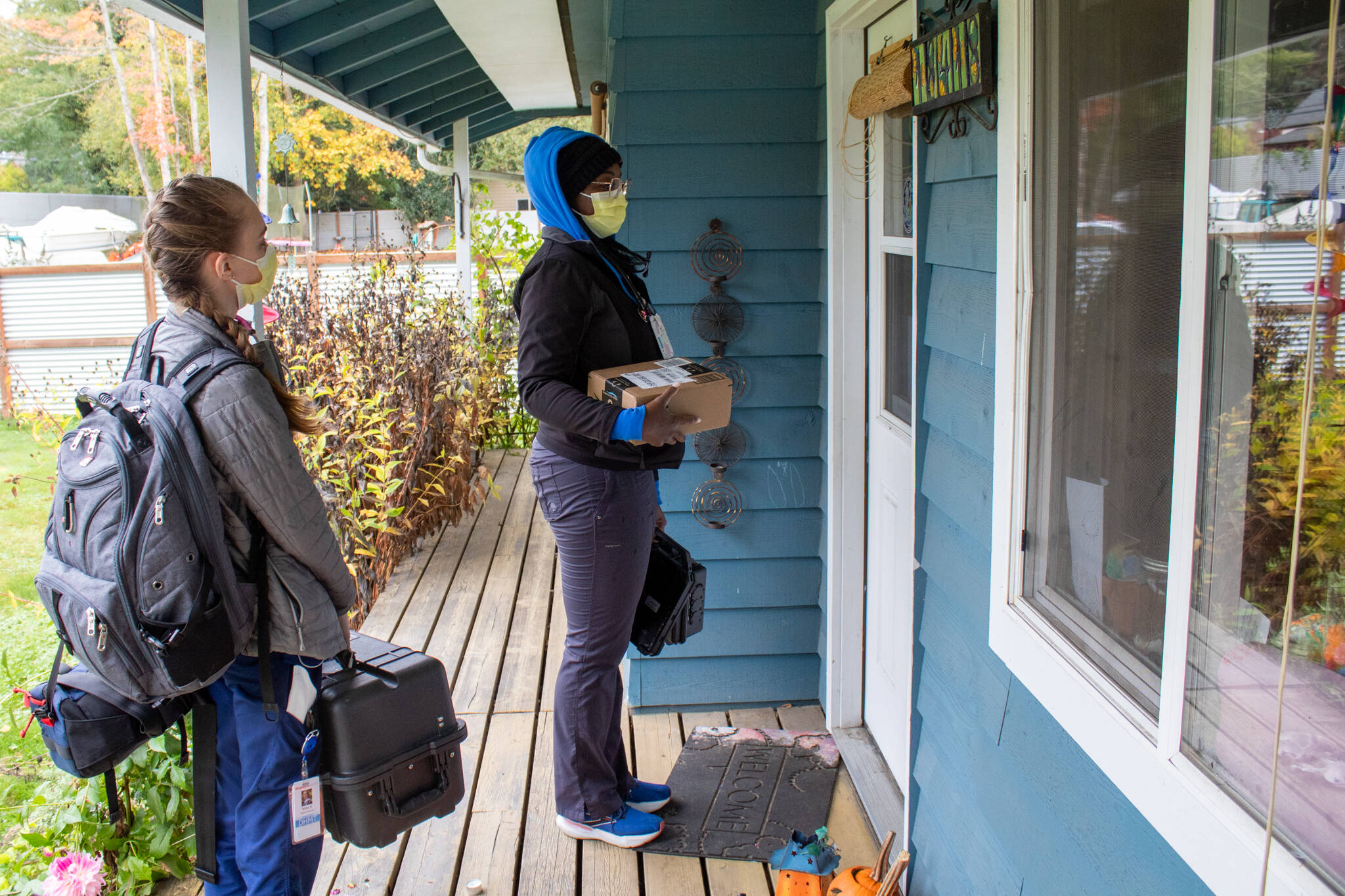 EMT Bailey Black and nurse practitioner Christian Graves wait to enter the home of a patient they’re seeing. Graves also holds an Amazon package left on the house’s porch, ready to hand it to the family inside. (Alex Bruell photo)